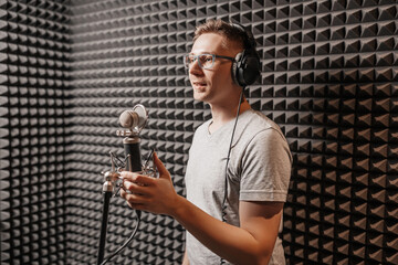 The vocalist sings in the studio in a microphone. Man in headphones writes a podcast, an audiobook. Artist, recording an album, working with the label. Announcer records a speech at a radio station - obrazy, fototapety, plakaty