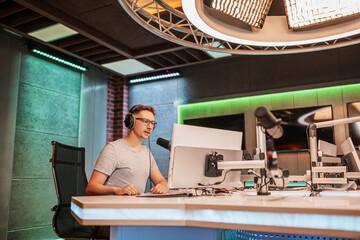 The DJ hosts the program and communicates with the audience on air at the radio station. The announcer reads the news. A male radio host speaks into a microphone and records a podcast