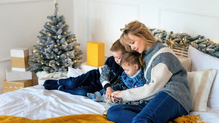 Mother with two sons laying on a bed against New Year background. Little boys with mom having fun celebrating Christmas at home.