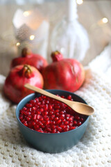 Bowl with fresh pomegranate seeds, pomegranate fruit, knitted blanket and lit candles. Hygge at home. Selective focus.