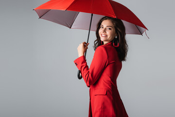 happy young woman in red suit standing under umbrella isolated on grey.