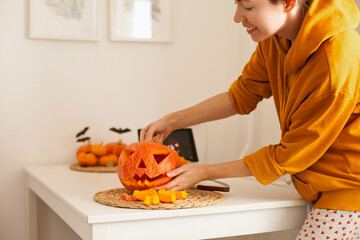 woman in yellow hoodie making a jack-o-lantern halloween pumpkin while watching tutorial online on tablet