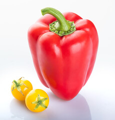 A beautiful young red bell pepper with a green stem and two beautiful yellow cherry tomatoes isolated on a white background