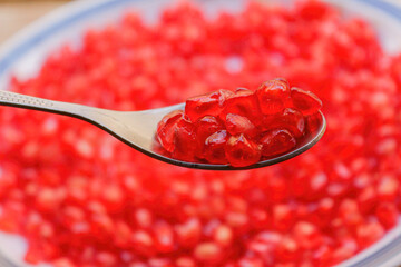 Closeup of pomegranate seeds on spoon isolated with background full of fresh pomegranate seeds, selective focus