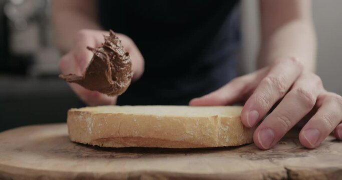 Slow motion spread nut chocolate paste on white bread on olive board