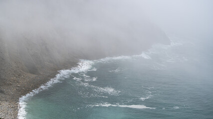 Mist over the sea. Fog over the water near a rock precipice. Mystical fog on the cliff of the ocean.