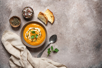 Pumpkin cream soup in a bowl with seeds and toast on a rustic brown background. Warm vegan winter soup. Top view, flat lay.