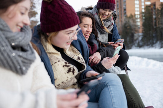 Happy young women friends using smart phones in winter park