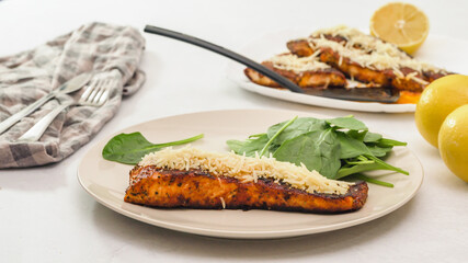 Smoked paprika roasted salmon served with Parmesan cheese, spinach and lemon  close up on a plate.