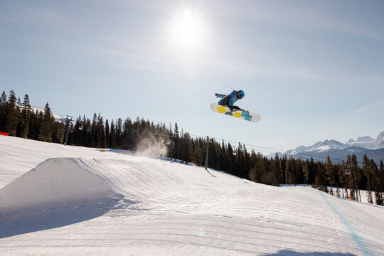 Snowboarder doing jump off ramp above sunny snowy mountain slope