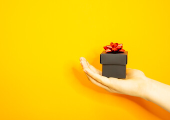 The girl's hand is holding a beautiful gift box. Makes a gift. Yellow background.