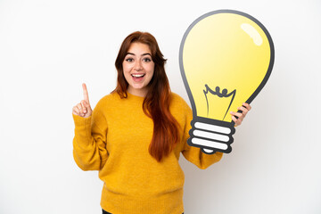 Young redhead woman isolated on white background holding a bulb icon and thinking