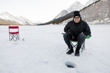 Portrait of cheerful man ice fishing on frozen alpine lake