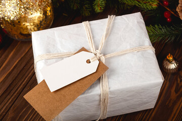 Christmas Gift Tag mockup. White minimal gift box on wooden table with festive decorations.
