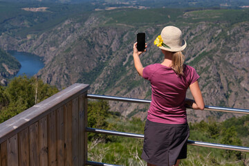 Fototapeta na wymiar Woman with hat photographing the Sil river canyon on her summer vacation