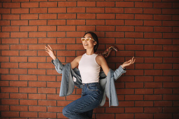 Gorgeous young asian brunette with gathered hair waving her arms to side on isolated background. Girl in sunglasses looks to side. Summer playful mood concept