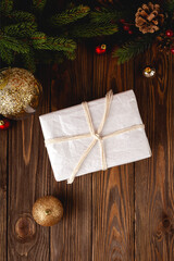 Minimalistic eco-friendly wrapped christmas gift on wooden table with fir tree branches and christmass balls.