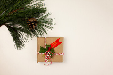 hand-made Christmas gift wrapped in craft paper and decorated with a sprig of holly on a white background. Christmas traditions. Winter holidays.