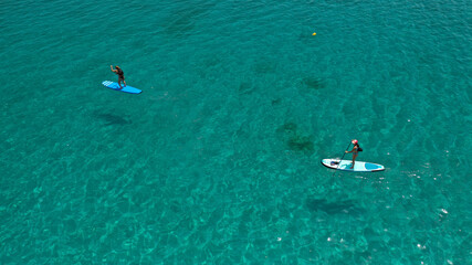 Aerial drone view of 2 women exercising sup board in turquoise tropical clear open sea