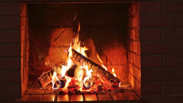 Burning logs and embers in a red brick fireplace in a country cottage on a dark cold evening 
