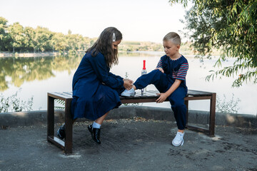 Little girl helps boy brother tie shoelace on bench in park. sister tying laces on shoes brother. Girl friend teaches kid to tie shoelaces. Love, friendship, helping concept