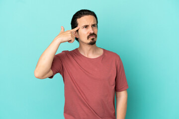 Young caucasian man isolated on blue background making the gesture of madness putting finger on the...