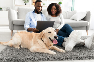 Black couple at home using pc laptop relaxing with dog