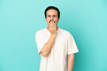 Young caucasian man isolated on blue background covering mouth with hand
