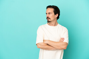 Young caucasian man isolated on blue background keeping the arms crossed