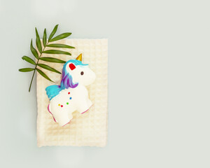 Baby bathing composition with a white towel, unicorn bath toy and palm leaf on a blue background with bubbles and copy space. Children bathing and baby care. Baby hygiene