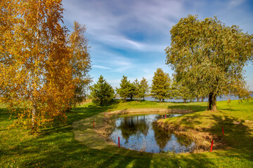 Fototapeta na wymiar Panorama of sunny autumn landscape with beautiful meadow and small pond on the banks of Kisezers lake in Riga, Latvia