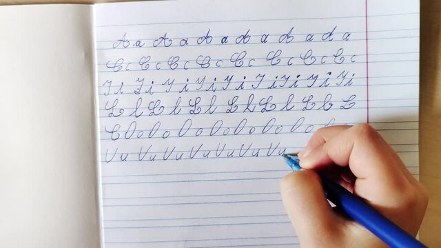 The child's hand writes french letters in a notebook. Child doing homework.
