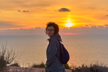 Fototapeta premium Hiker woman looking at camera while sunrise at sea