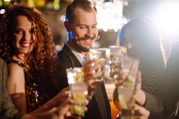 Cheering and drinking cocktails. Group of friends partying in a nightclub and toasting drinks with cocktails. Happy people enjoying winter holiday. Party, celebration, drink, birthday concept.