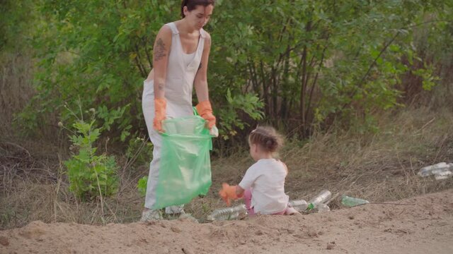 Little girl helps mother collects plastic garbage on nature to save environment from pollution Kid collecting plastic trash waste bottles volunteer teamwork Save the Planet caring about environment. 