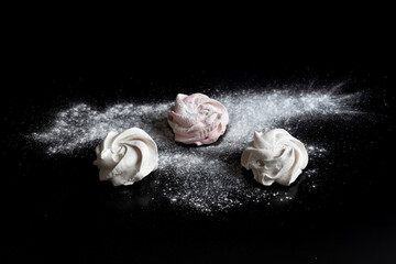 An airy marshmallow sprinkled with powdered sugar on a black background. Selective focus