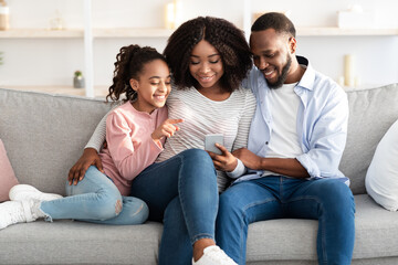 Happy african american family holding and using cellphone at home