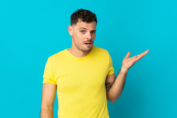 Young caucasian handsome man isolated on blue background making doubts gesture
