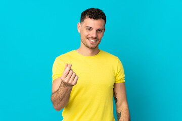 Young caucasian handsome man isolated on blue background making money gesture