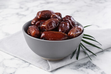 Sweet dried dates in bowl on white marble table, closeup