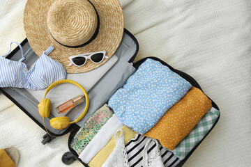 Open suitcase full of clothes and summer accessories on bed, flat lay
