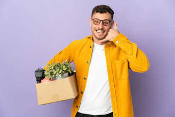 Young caucasian man making a move while picking up a box full of things isolated on purple...
