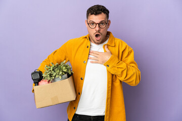 Young caucasian man making a move while picking up a box full of things isolated on purple...