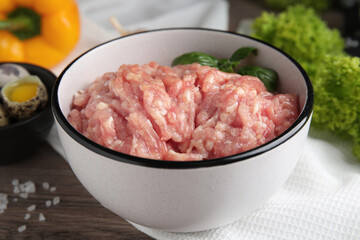 Raw chicken minced meat with basil on wooden table, closeup