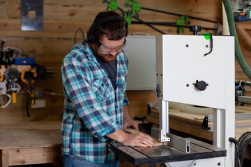  A carpenter in a plaid shirt works at a machine in a workshop. Wood. Ecological compatibility. Lifestyle.