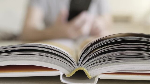 Open book close-up and in blurred background man with smartphones taking picture and making cheat sheet