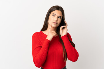 Teenager Brazilian girl using mobile phone over isolated white background having doubts while looking up