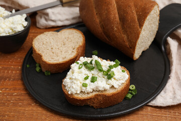 Bread with cottage cheese and green onion on wooden table, closeup