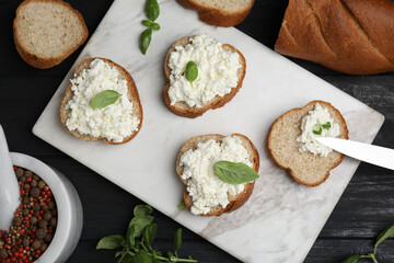 Bread with cottage cheese and basil on black wooden table, flat lay