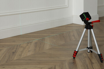 Cross line laser level with tripod on wooden floor indoors - Powered by Adobe